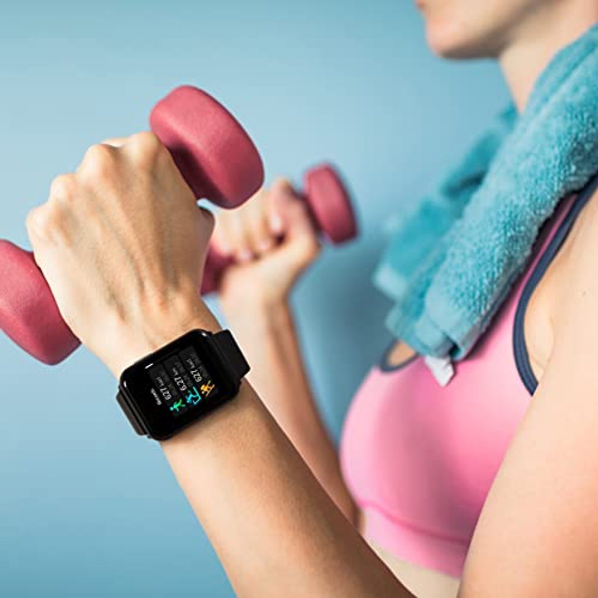 Frau trainiert mit Kurzhanteln, trägt ein rosa Oberteil. Eine Smartwatch befindet sich an ihrem Handgelenk, zeigt Fitnessdaten.