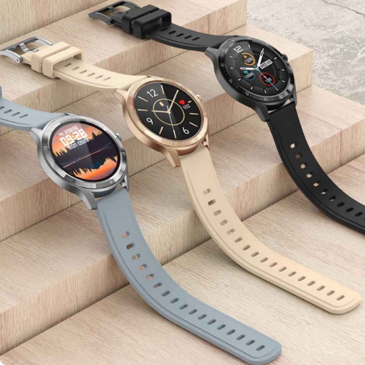 Trzy smartwatche z paskami w różnych kolorach. Leżą na drewnianej powierzchni.