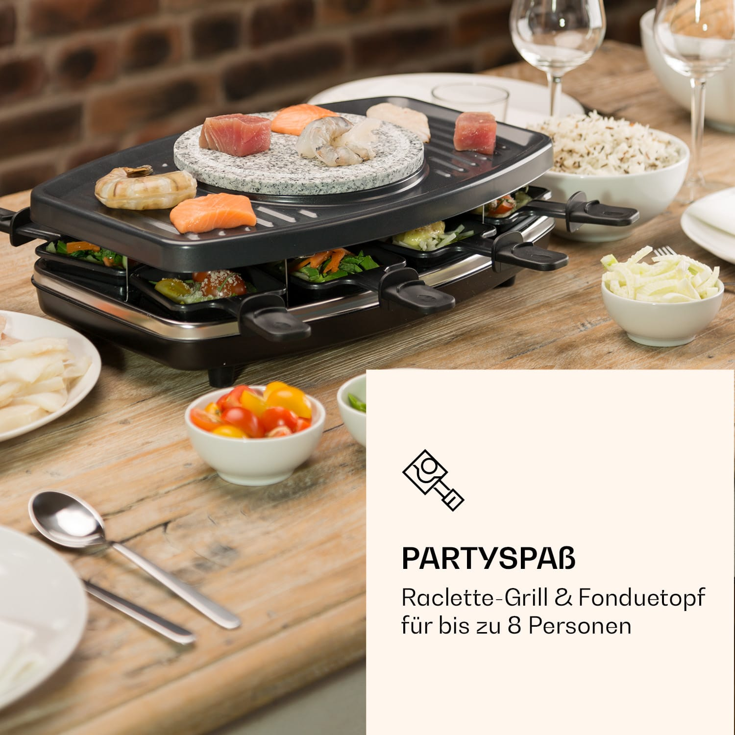 Ein Raclette-Grill mit Essen darauf, mit Tellern, Löffeln und Schalen mit Essen auf dem Tisch.