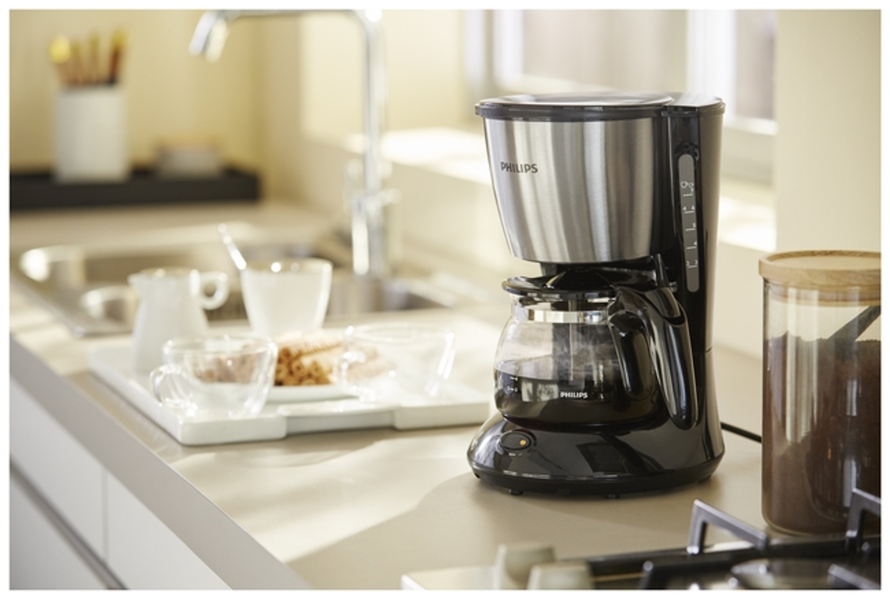 Czarno-srebrny ekspres do kawy na blacie kuchennym, z filiżankami i tacą w tle.