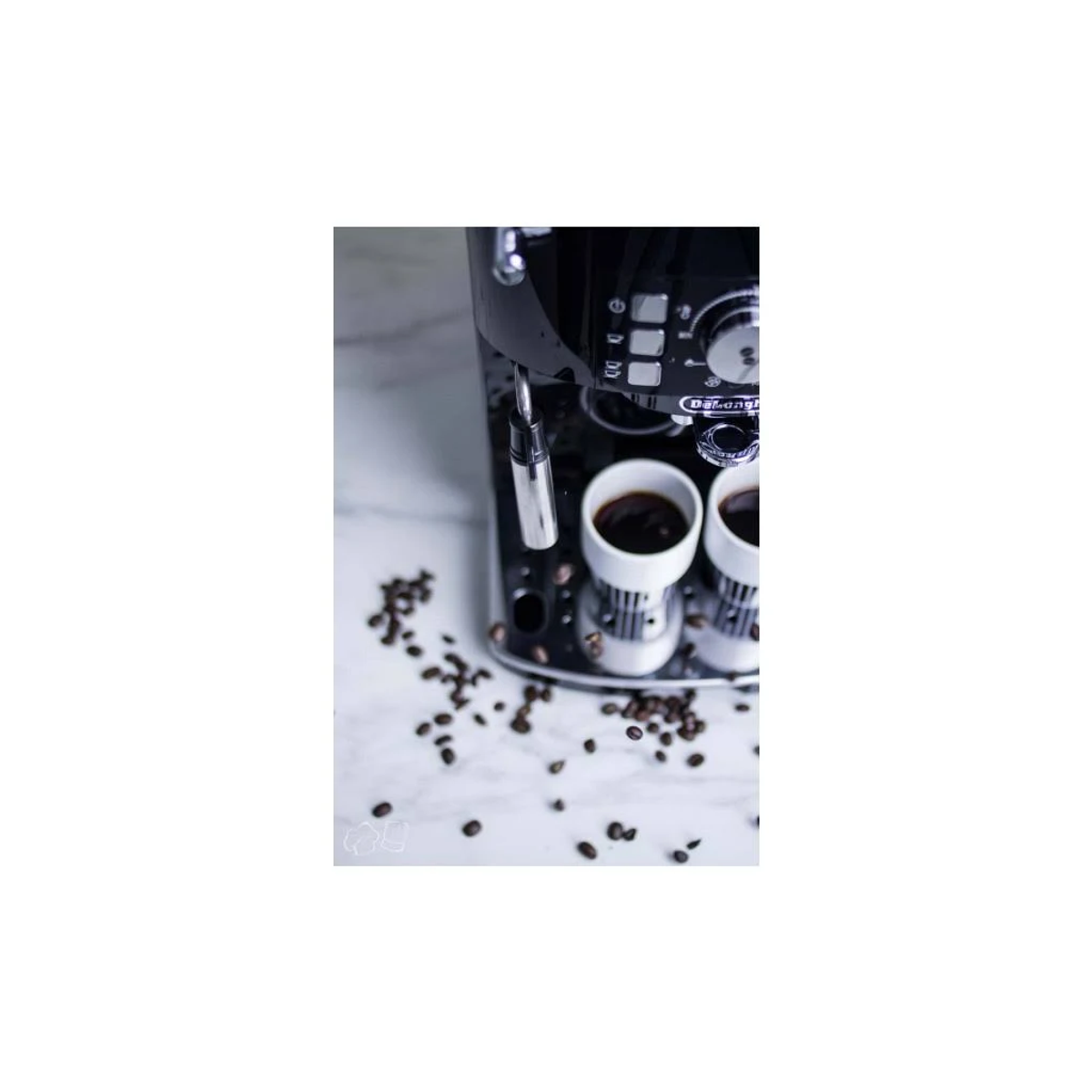 Czarny ekspres do kawy z dwoma filiżankami, rozsypane ziarna kawy, na marmurze.