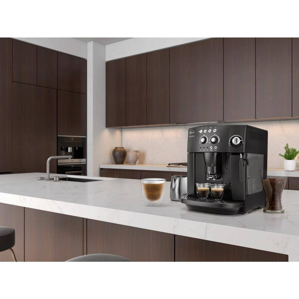 Máquina de espresso negra sobre una encimera blanca en una cocina. Un vaso de café y granos de café al lado.