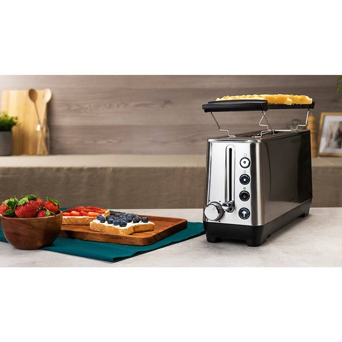 Toster ze stali nierdzewnej z wyskakującym tostem. Truskawki i chleb z dodatkami w pobliżu.