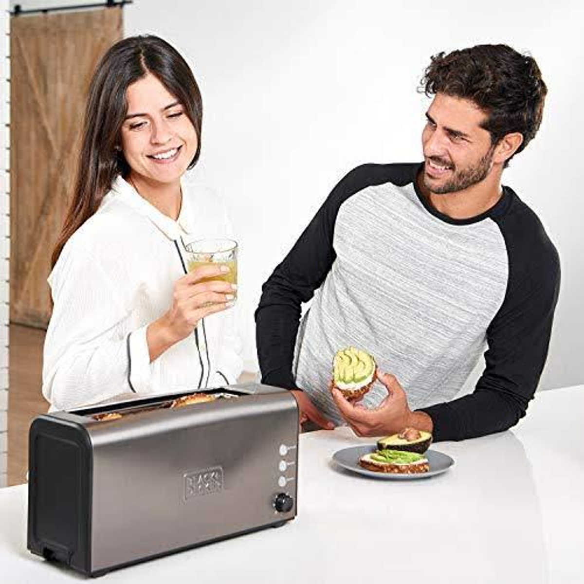 Hombre y mujer en cocina. Tostadora en el mostrador. Hombre con tostada de aguacate.