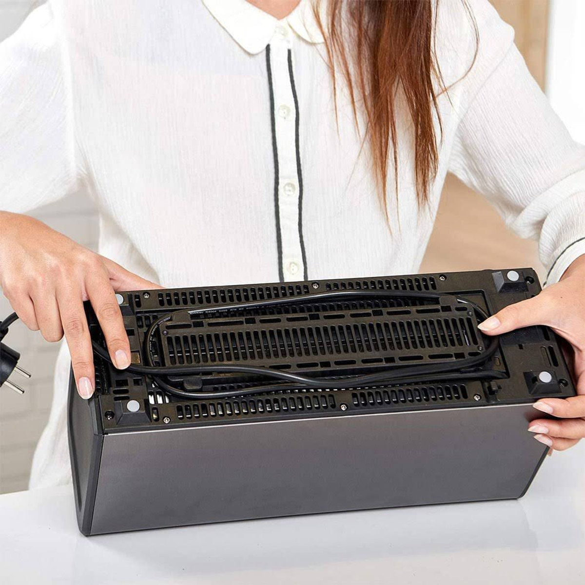 Persona sosteniendo un dispositivo negro con un cable de alimentación. El dispositivo está sobre una mesa blanca.