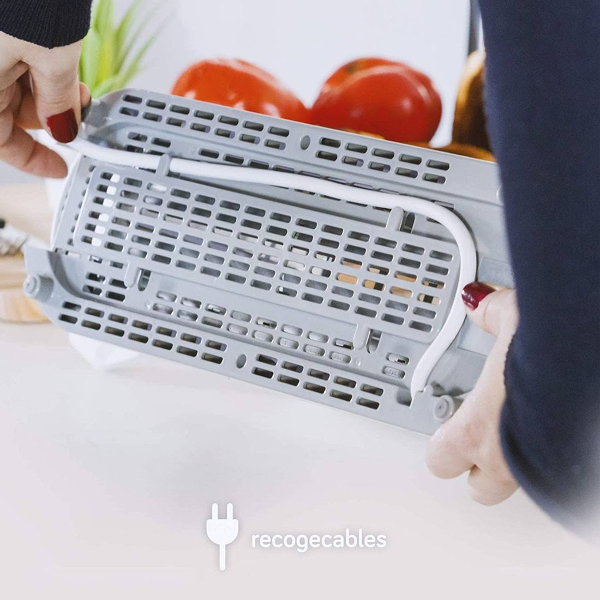 Ręce osoby składającej szarą frytkownicę powietrzną z widocznym białym przewodem zasilającym.