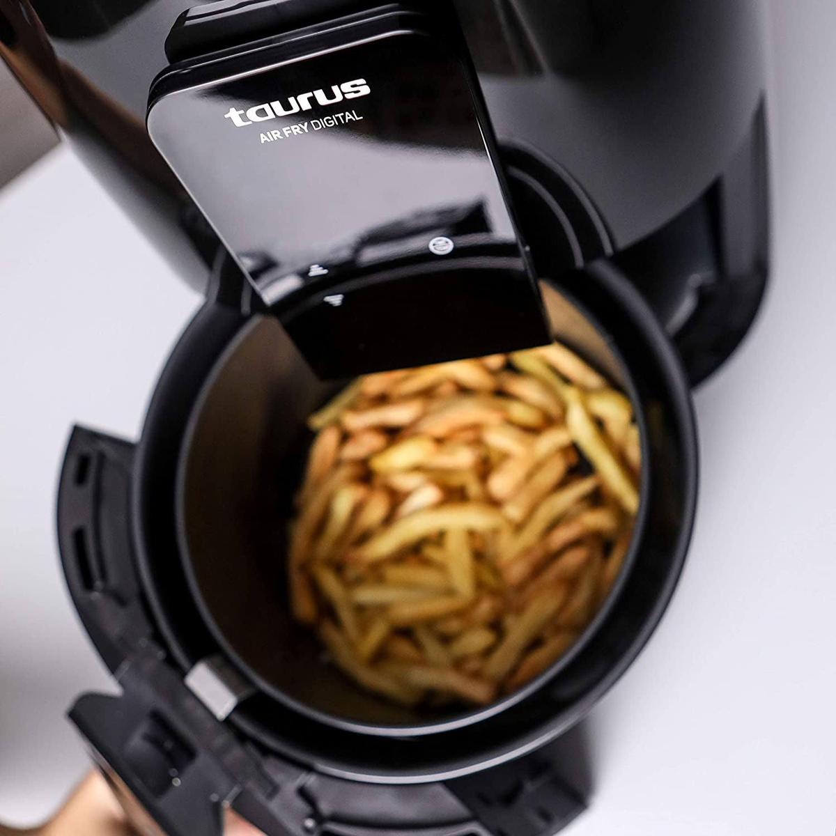 Freidora de aire negra con cesta abierta llena de patatas fritas.