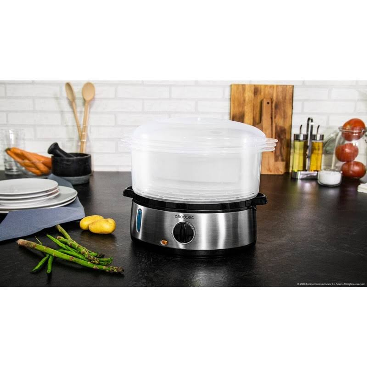 Vaporiera argento e nera con coperchio trasparente, asparagi e patate sul bancone.