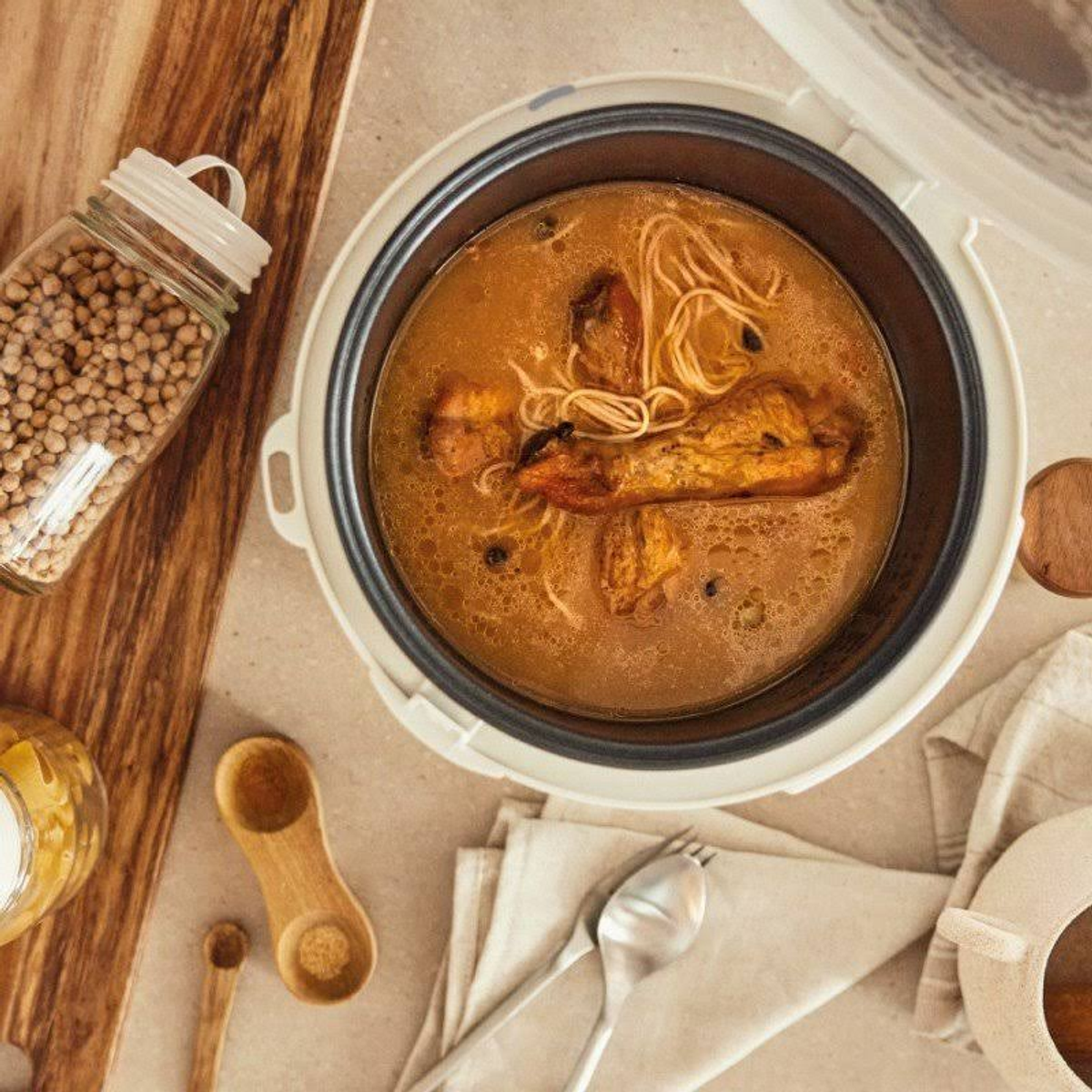 Vista cenital de una arrocera con comida y utensilios en la mesa. La comida está en la olla.