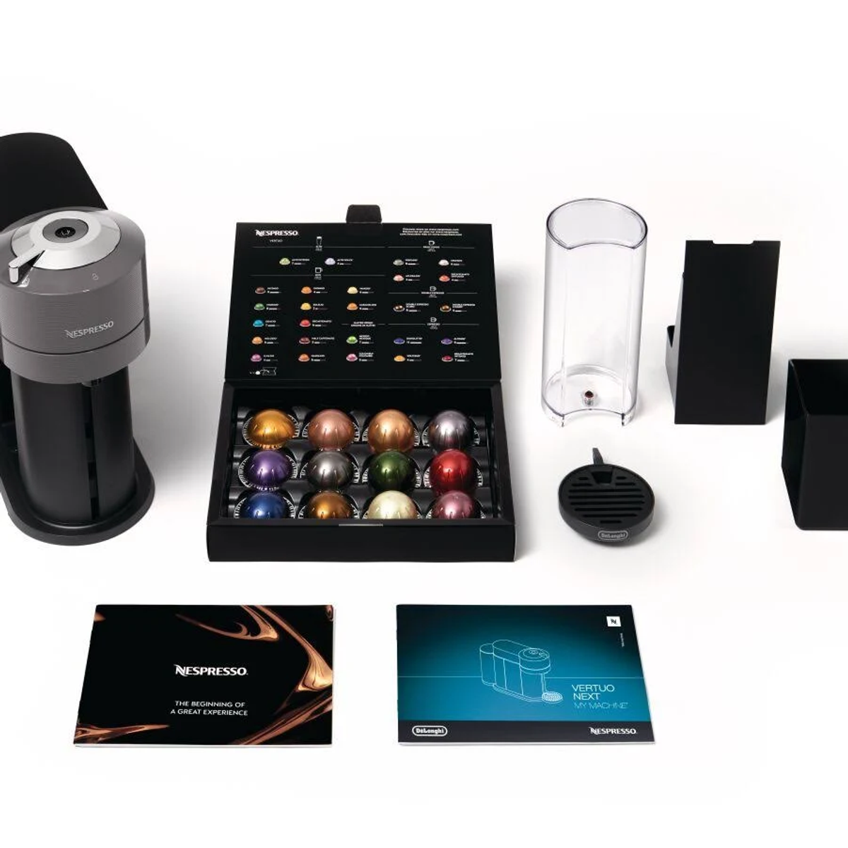 Macchina Nespresso con capsule, accessori e scatola, tutto su superficie bianca.