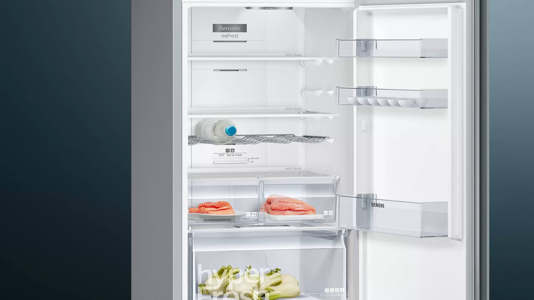 Interior de refrigerador. Estantes, cajones con alimentos. Botella de agua. Interior blanco con luz.