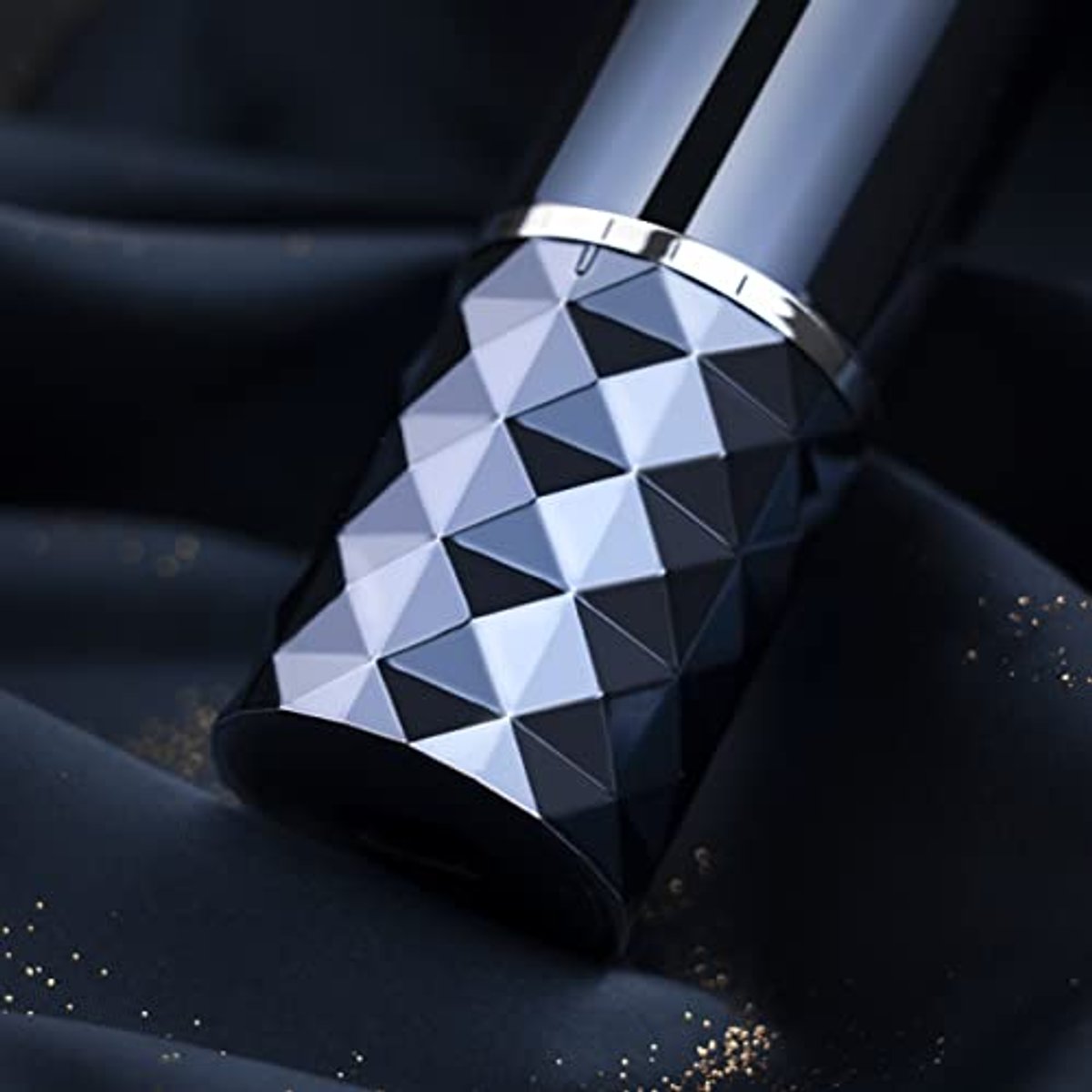 Schwarze und silberne Parfümflasche mit geometrischem Muster auf dunklem Stoffhintergrund.