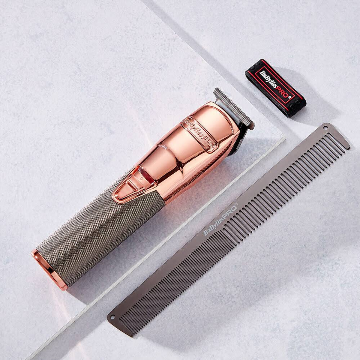 Ein Haarschneider und Kamm auf weißer Oberfläche. Der Haarschneider ist roségoldfarben und hat ein Babyliss Pro-Etikett.