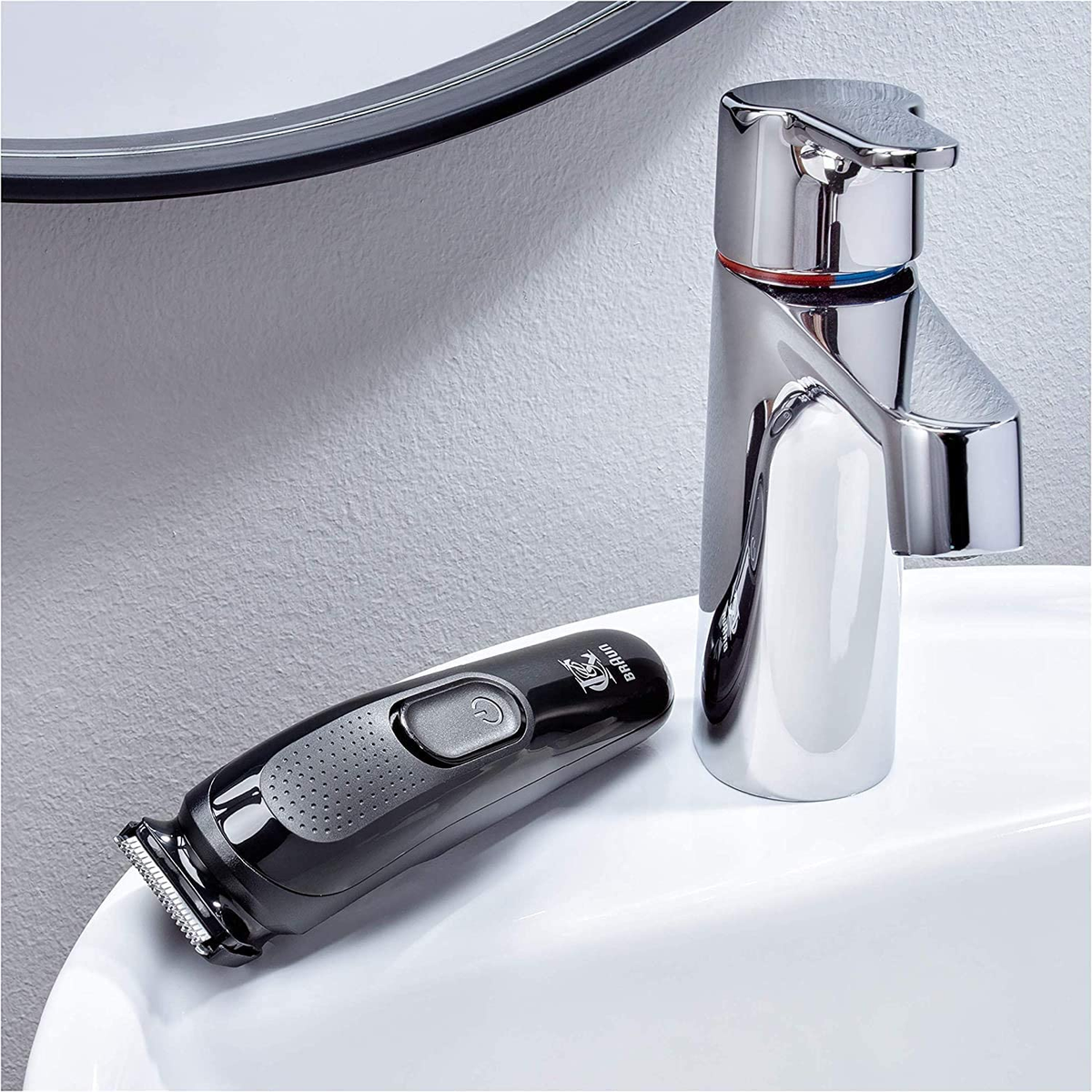 Schwarzer Rasierer und verchromter Wasserhahn auf einem weißen Waschbecken.