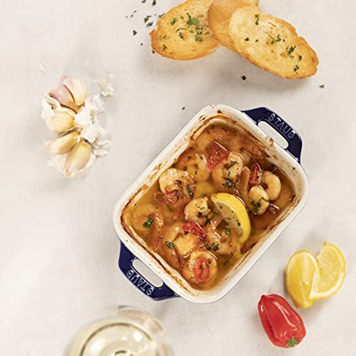 Draufsicht auf eine weiße Schüssel mit Garnelen und Zitrone in Sauce mit Knoblauch, Zitronen und Brot.