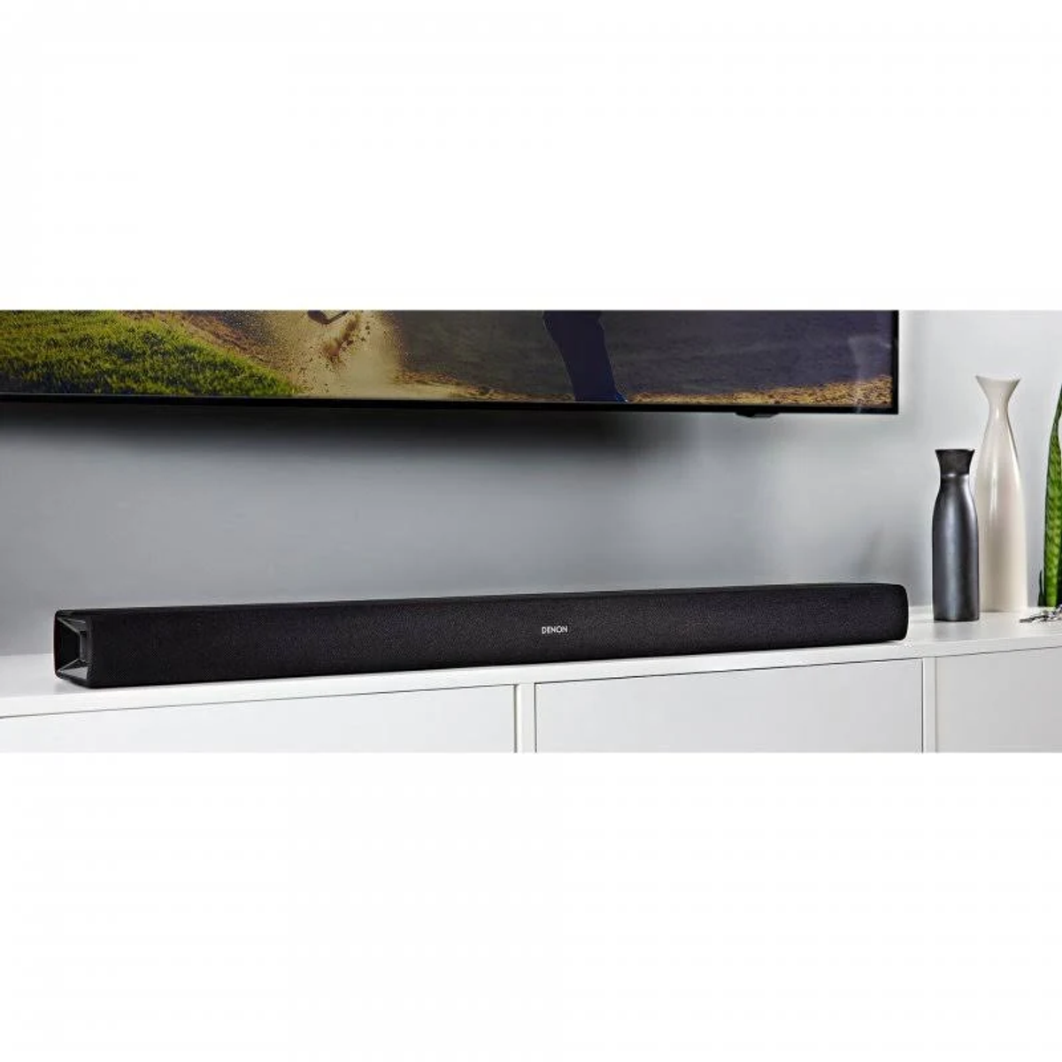 Schwarze Soundbar auf einem weißen Schrank, darüber ein Fernseher.