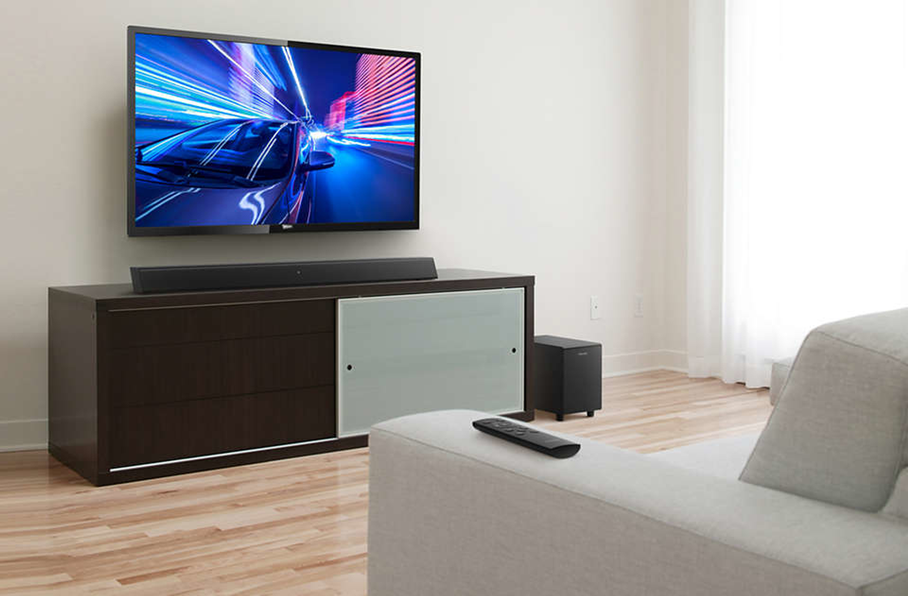 Scena di soggiorno con TV, soundbar e divano. La TV mostra una scena di corse automobilistiche.