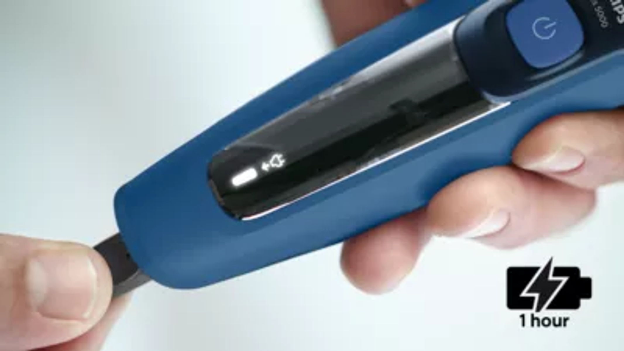 Męskie dłonie w pobliżu niebieskiej golarki elektrycznej Philips, pokazujące ikonę ładowania.