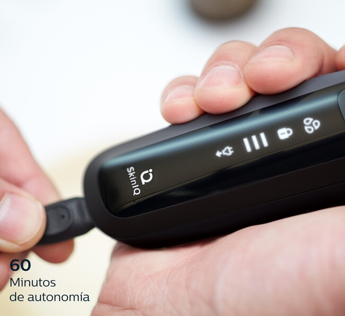 Una persona che collega un cavo di ricarica a un rasoio nero, mostrando la durata della batteria e il tempo di utilizzo: 60 minuti.