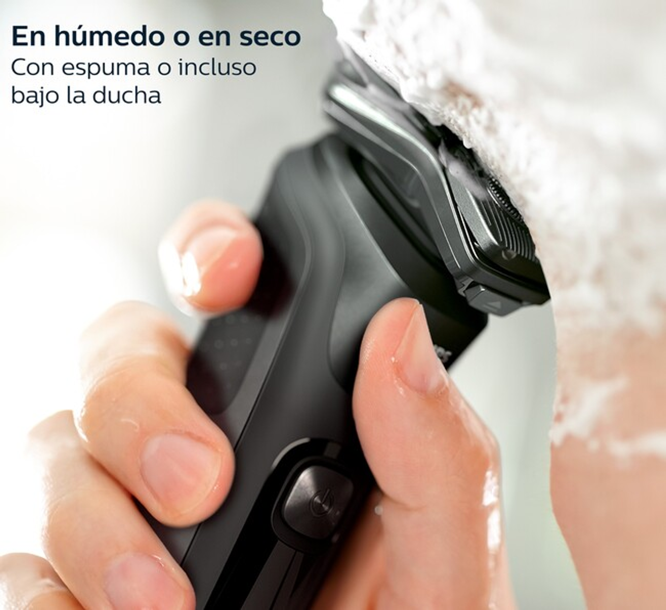 Una mano rade un viso con un rasoio elettrico nero e schiuma da barba bianca sullo sfondo.