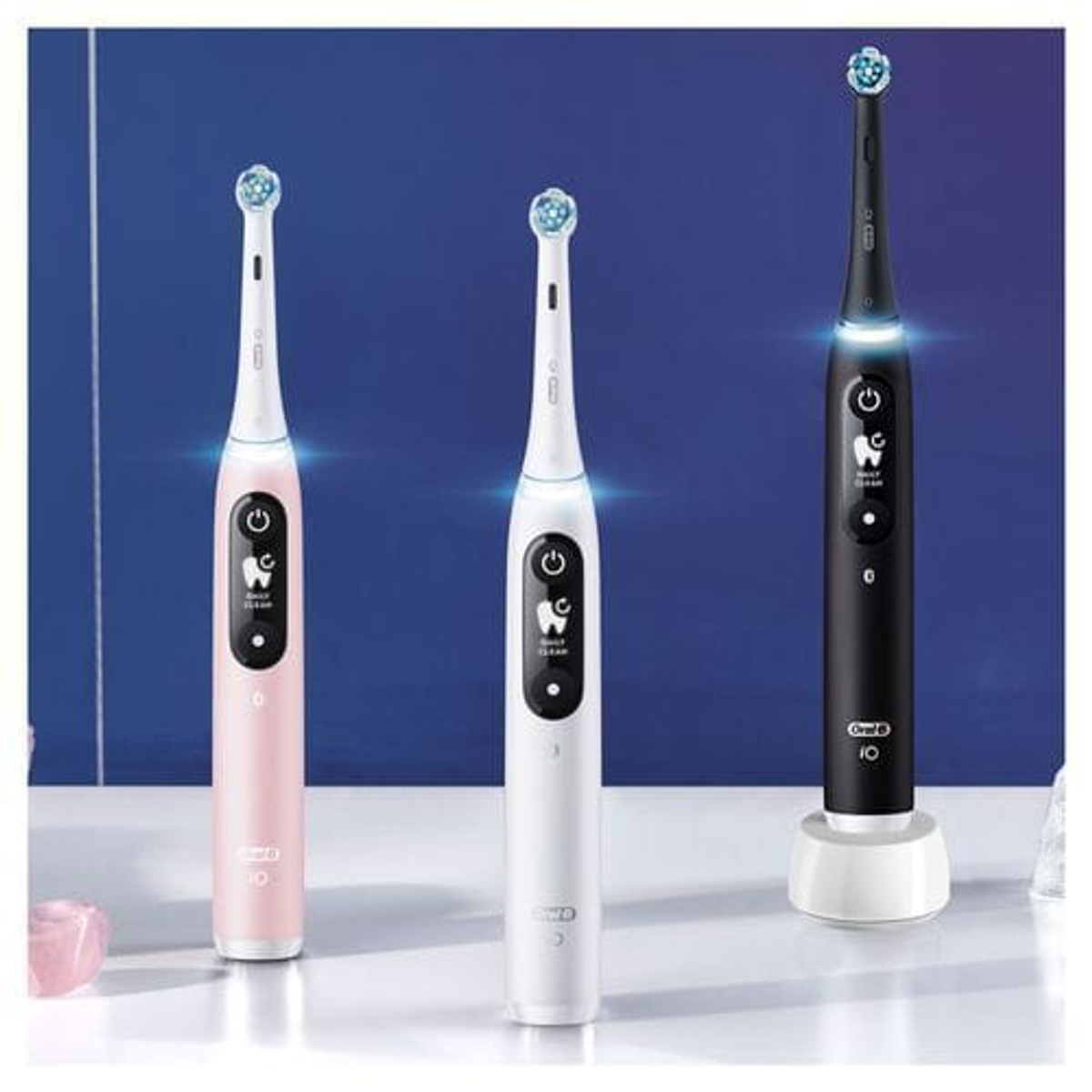 Tres cepillos de dientes eléctricos con diferentes colores sobre una superficie blanca.