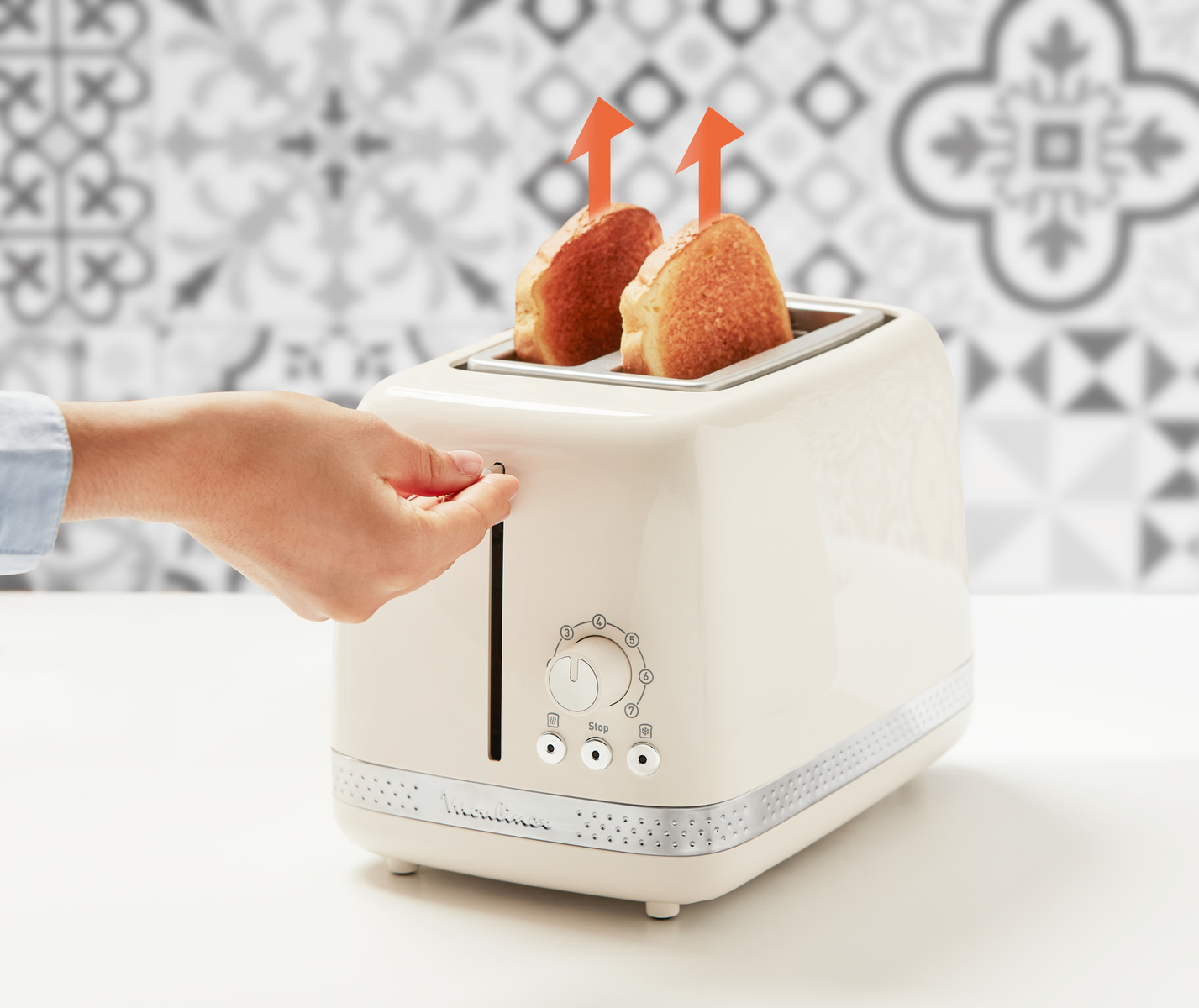 Ręka wyciąga tost z beżowego tostera z dwoma kromkami tostów.