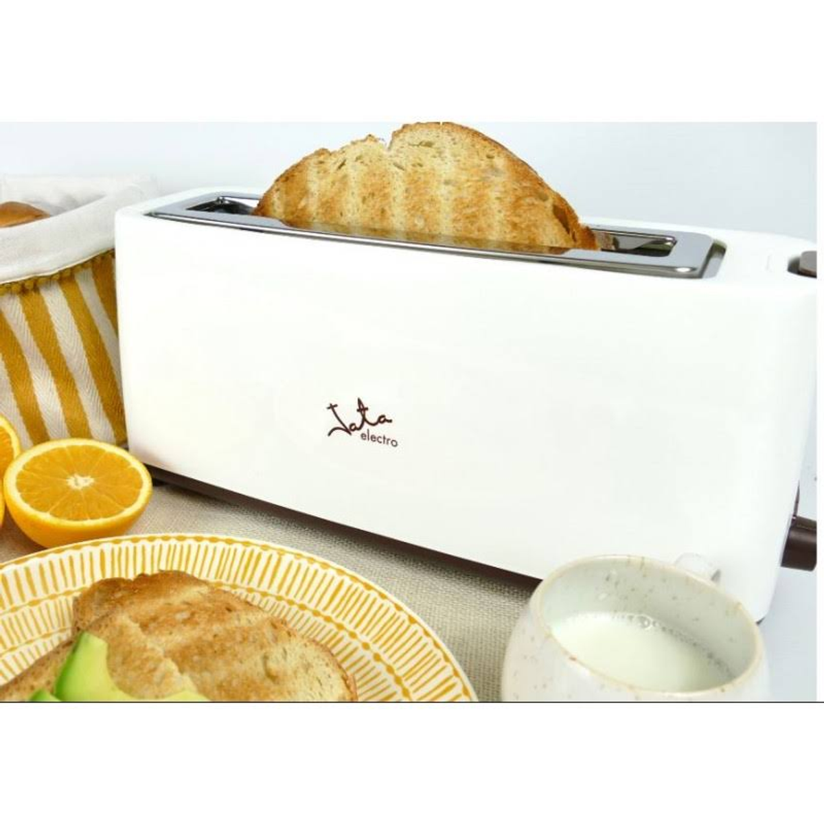 Biały toster z kromkami chleba, pomarańczą i innymi produktami śniadaniowymi na stole. Marka to 'Jata electro'.