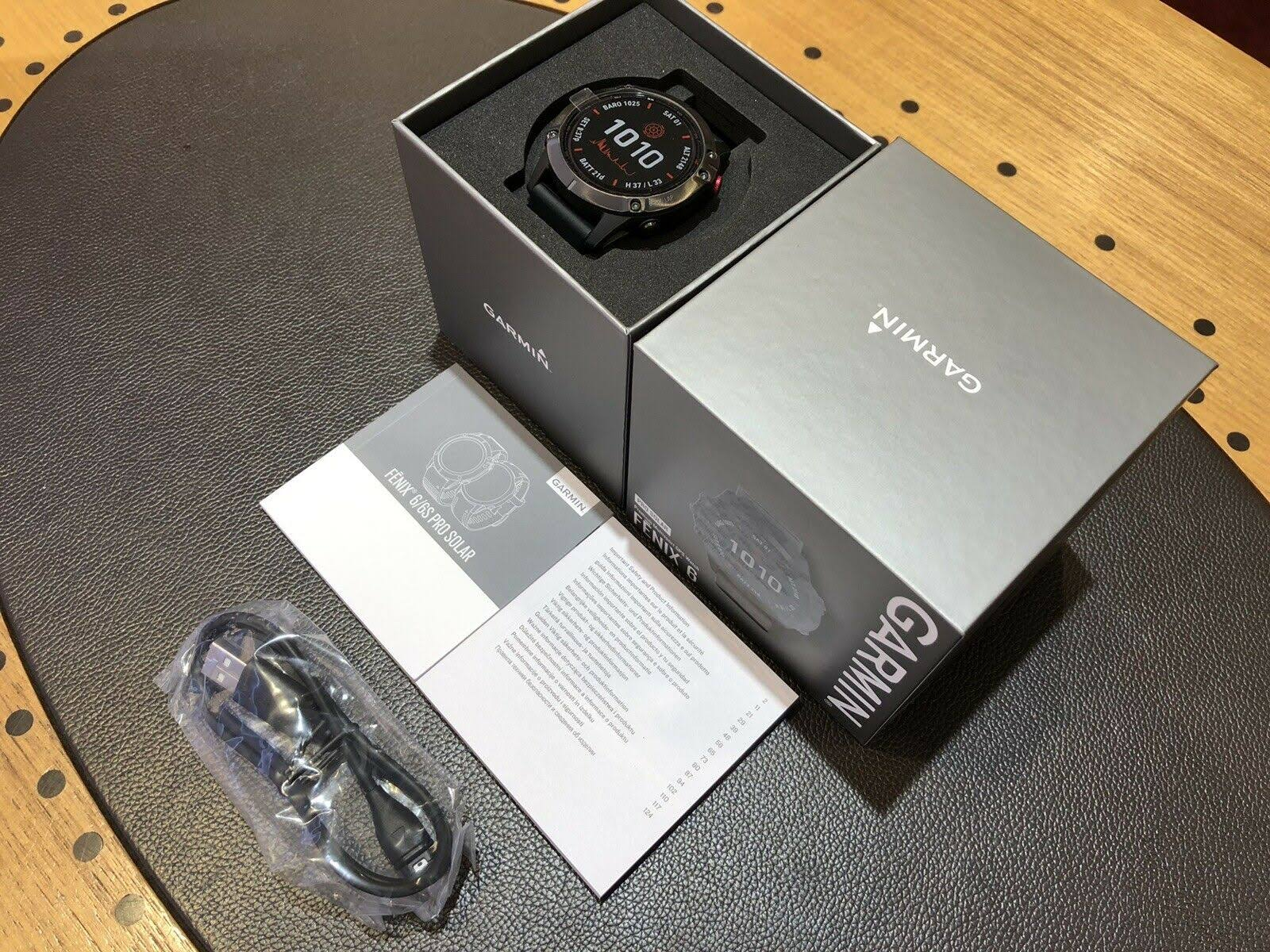 Garmin-Uhr in der Box, Handbuch und Ladekabel auf einem Tisch.
