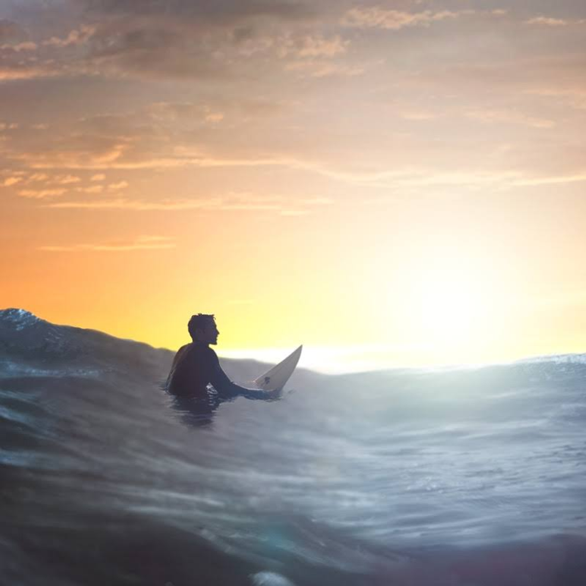 Ein Surfer sitzt auf einem Surfbrett im Wasser bei Sonnenuntergang.