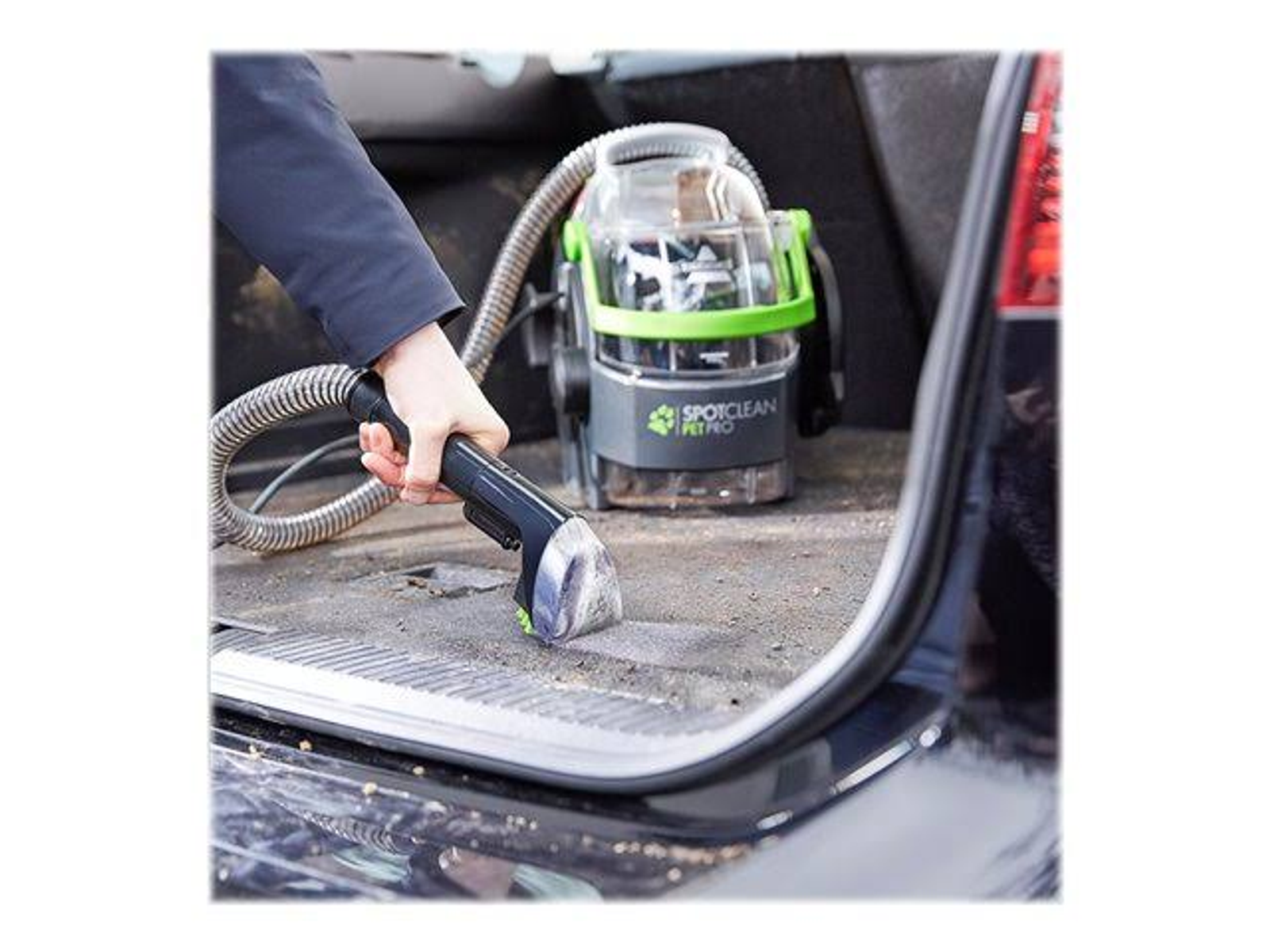 Una mano usando un SpotClean Pet Pro en el piso de un automóvil, aspirando un área sucia.