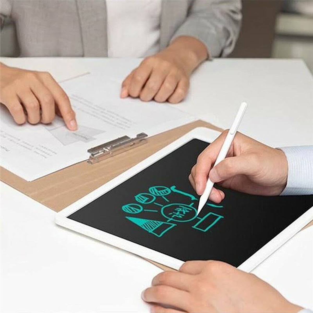 Deux personnes à une table, l'une pointe un document, l'autre dessine sur une tablette avec un stylet.