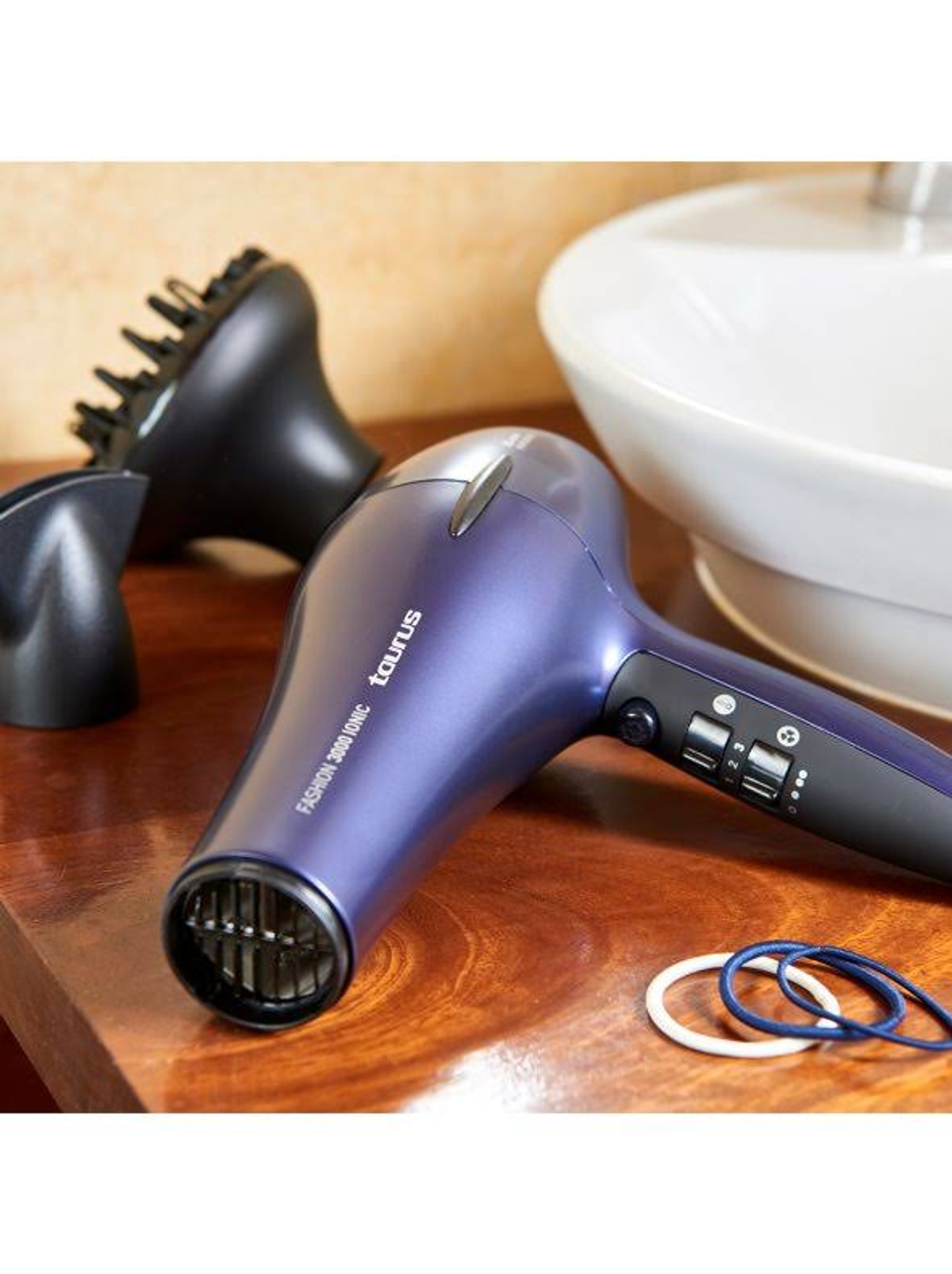 Suszarka do włosów przed lustrem i umywalką. Dwa nasadki i gumki do włosów są obecne.