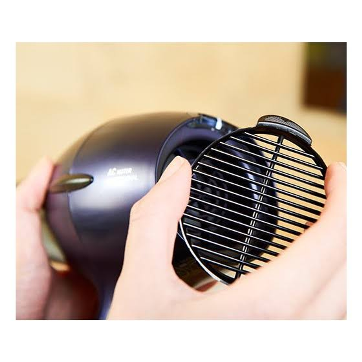 Dłonie trzymające czarną suszarkę do włosów, usuwające czarny filtr z białymi paskami.