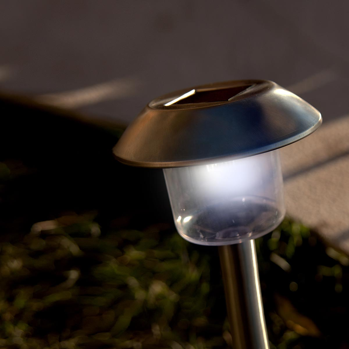 Ein Solar-Gartenlicht mit klarem Oberteil, das hellweißes Licht aussendet, in einem Garten aufgestellt.