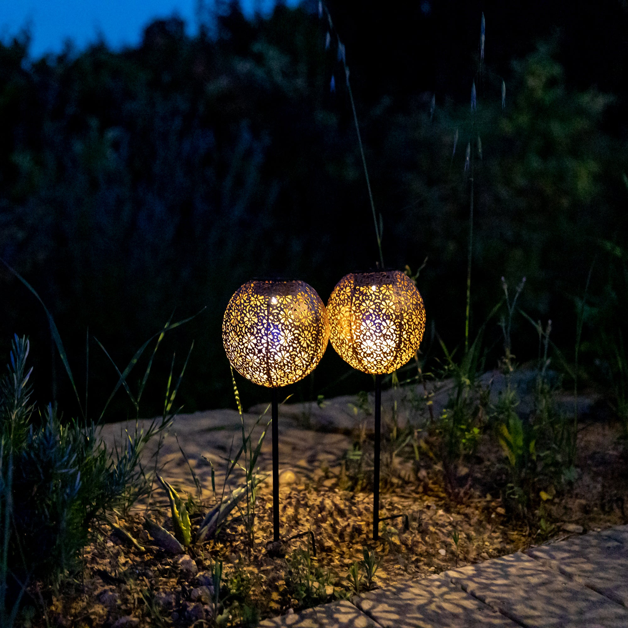 Zwei leuchtende kugelförmige Außenleuchten in einem Garten bei Nacht.