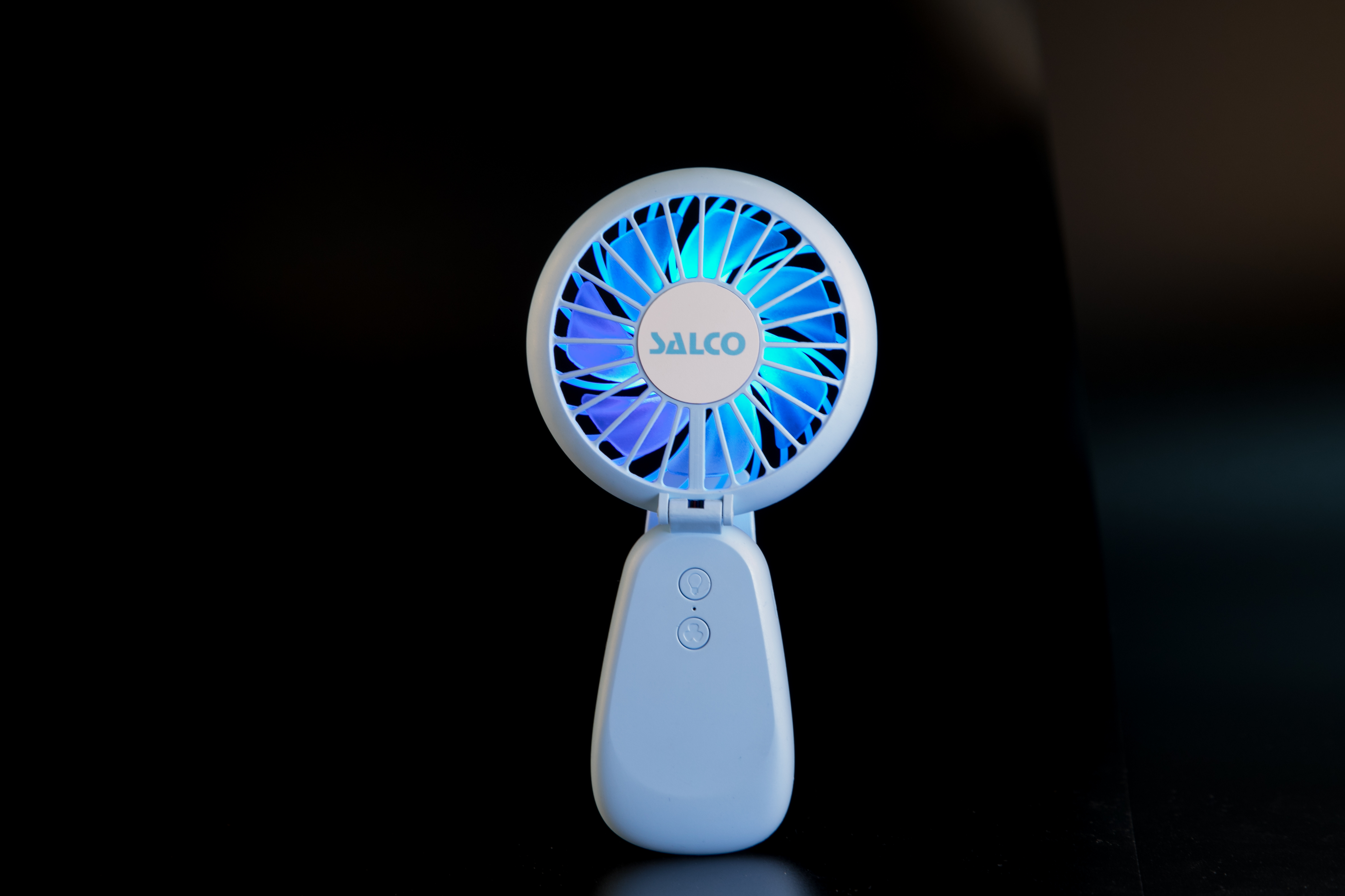 Hellblauer, tragbarer Ventilator mit blau leuchtenden Flügeln auf schwarzem Grund.