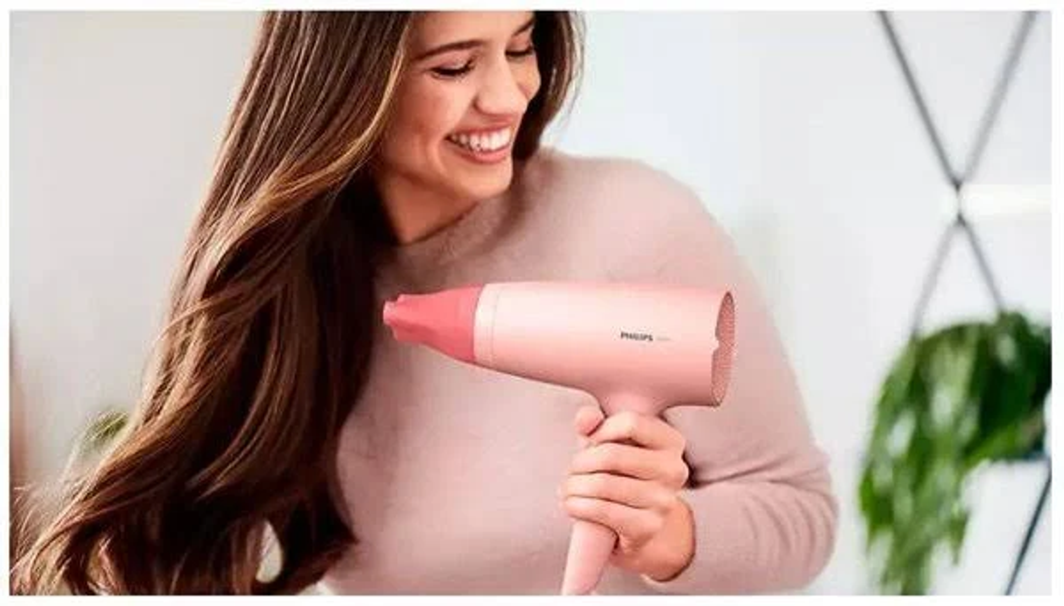Donna con capelli lunghi sorridente, che tiene un asciugacapelli rosa.
