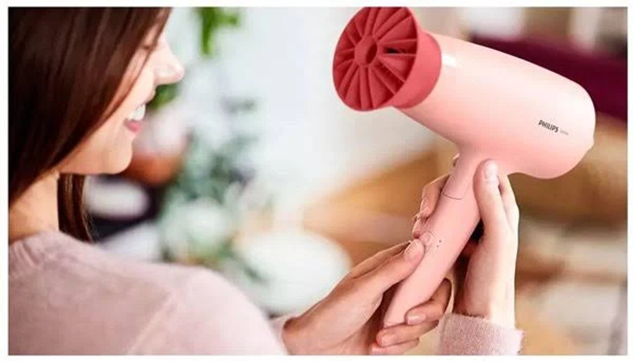 Donna che tiene un asciugacapelli rosa. L'asciugacapelli ha un ugello rosso. Sfondo sfocato.