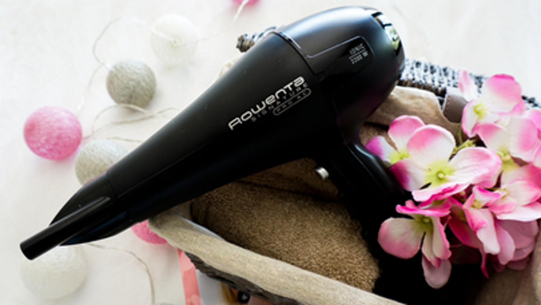 Czarna suszarka do włosów w koszu z różowymi kwiatami i białymi światłami.
