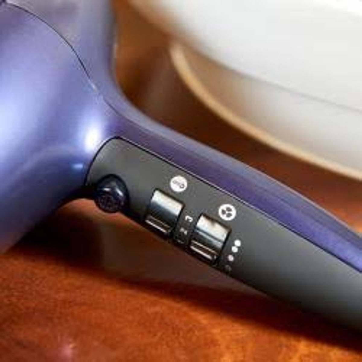 Un secador de pelo morado con controles negros está sobre una mesa de madera, cerca de un objeto blanco.