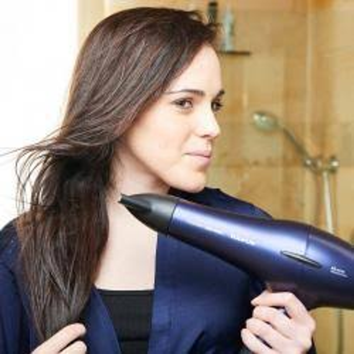 Mujer con pelo largo castaño usando un secador de pelo azul.