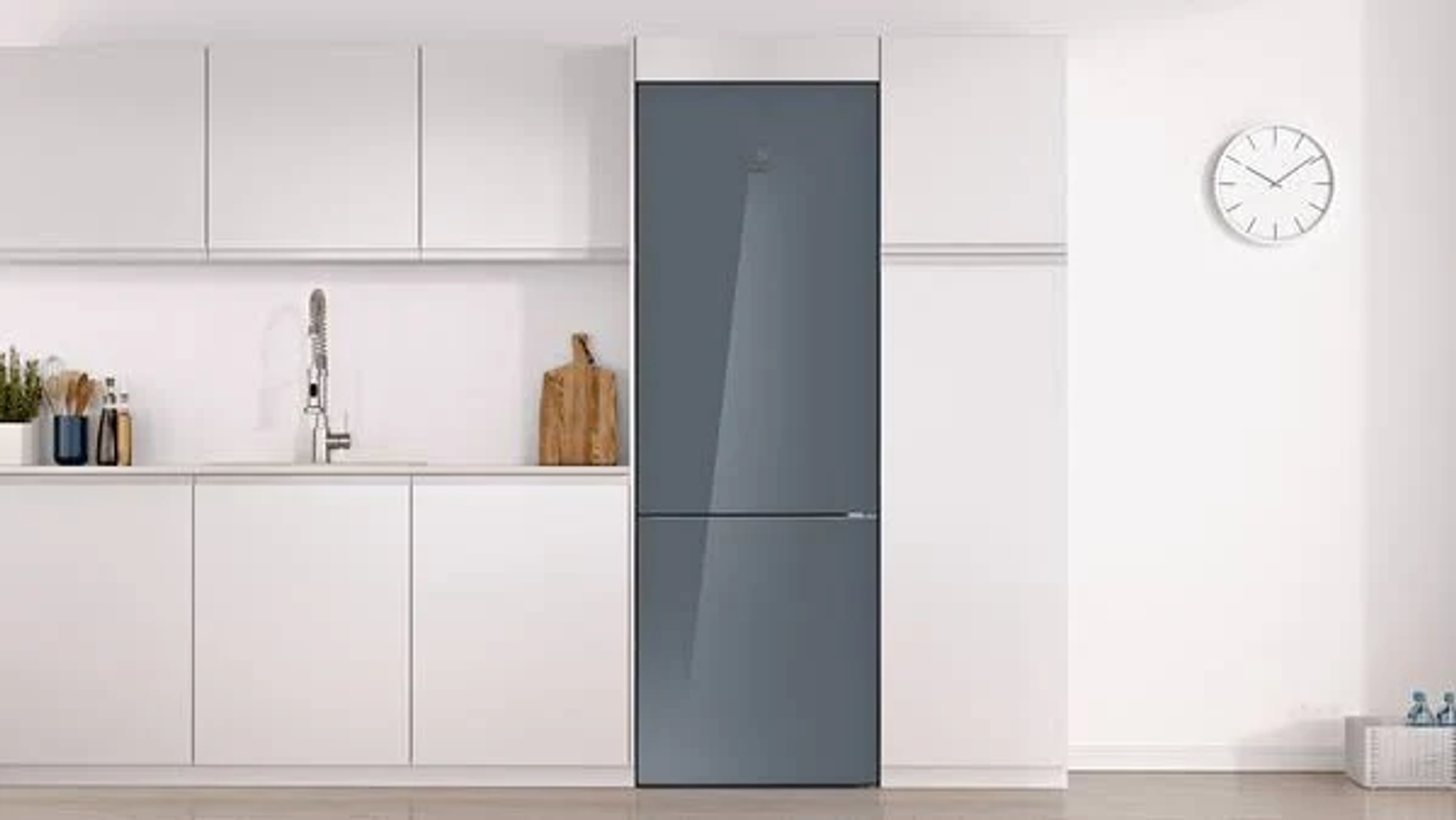 Frigorífico moderno con puerta gris oscuro. Está en una cocina blanca. Se ven un reloj y una tabla de cortar.