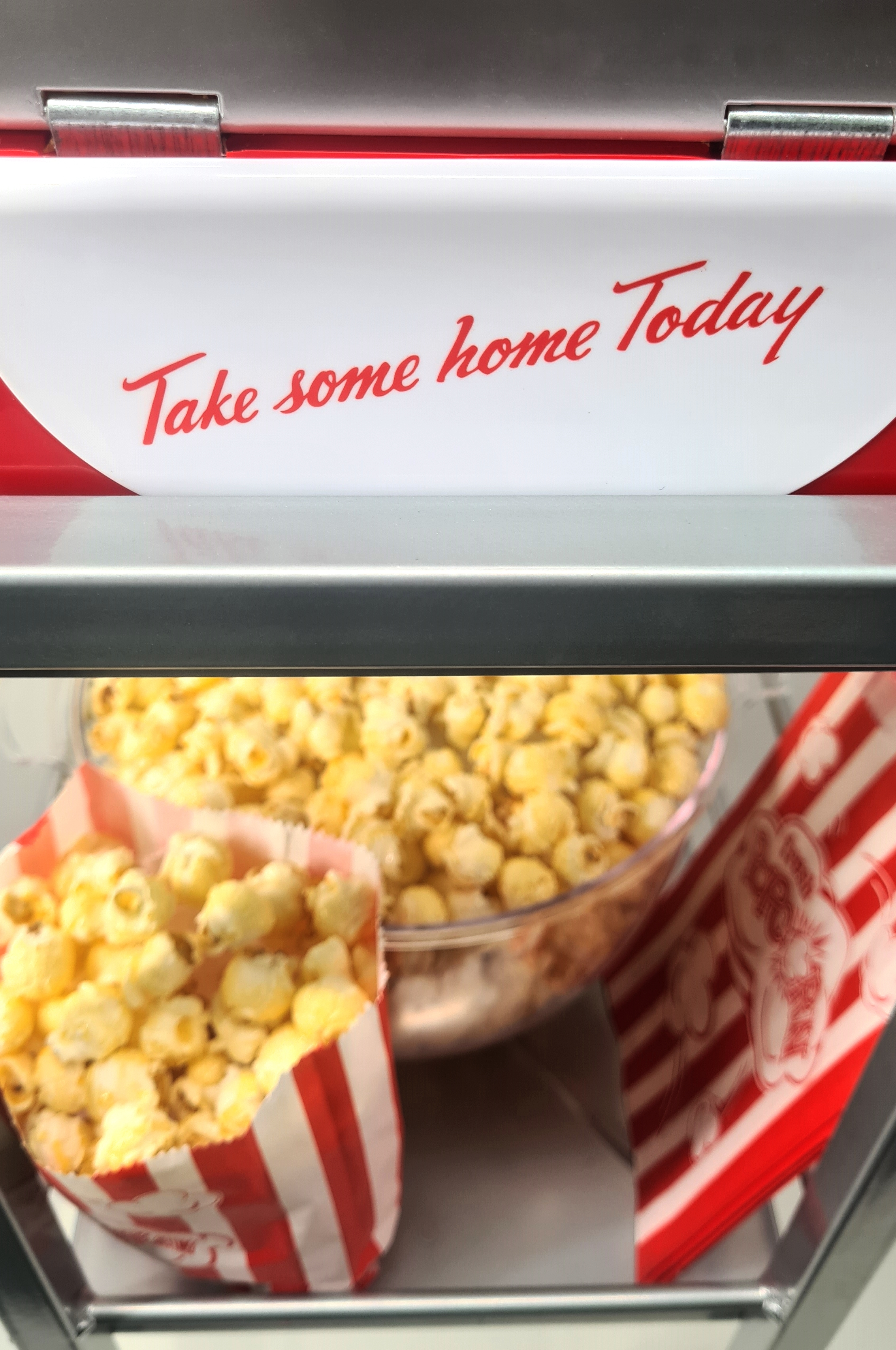 Eine Popcornmaschine mit Popcorn in einer Schüssel und Tüten. Das Schild sagt: 'Take some home Today'.