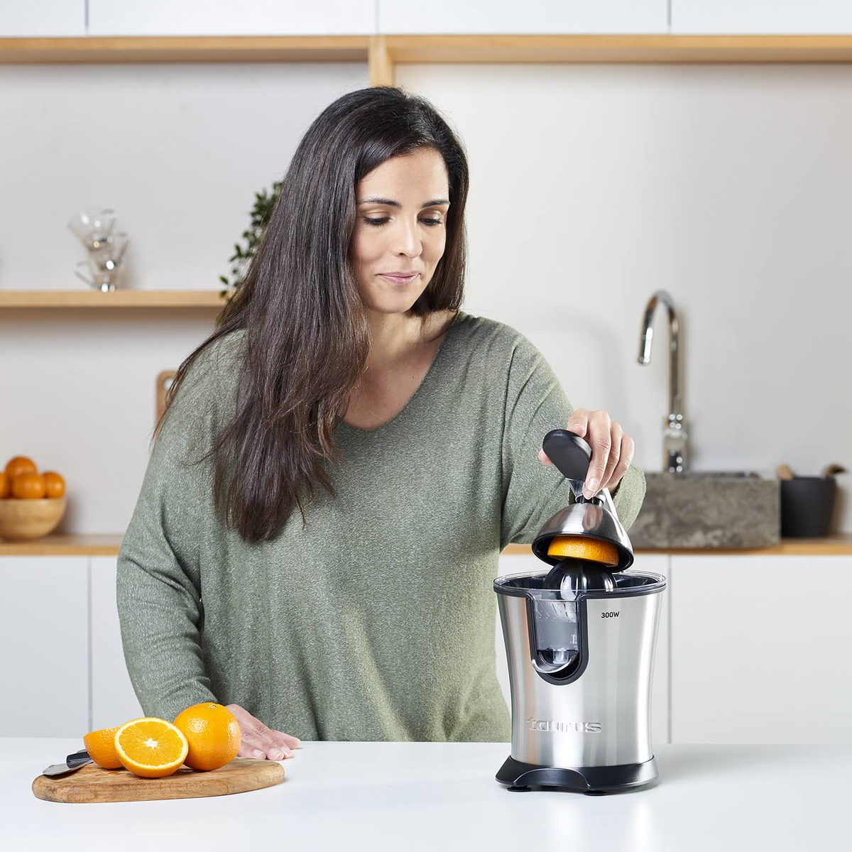 Mujer usando una exprimidora Taurus. Exprime media naranja. Ambiente de cocina, encimera blanca.