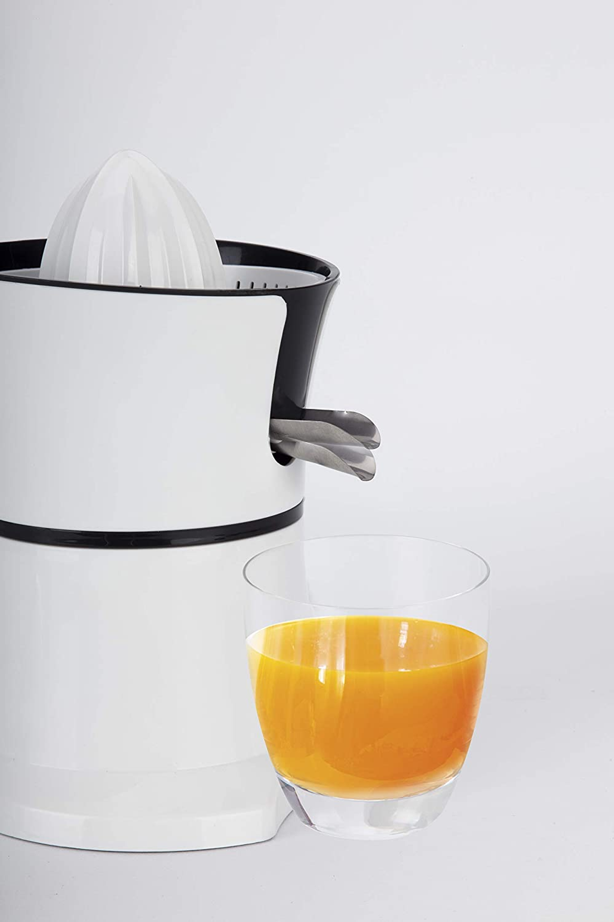 Una exprimidora de cítricos blanca y negra con un vaso de zumo de naranja al lado.