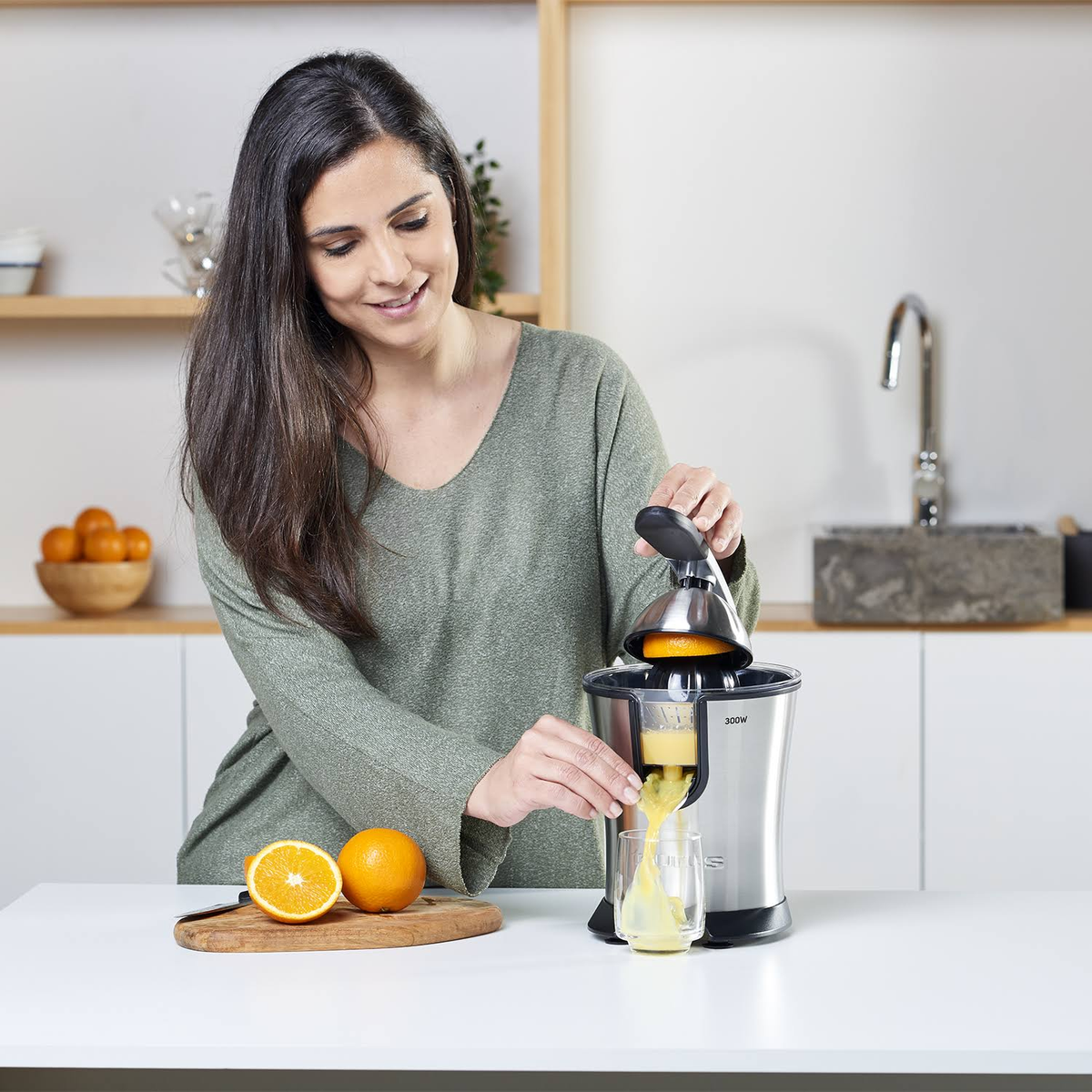 Una mujer exprimiendo una naranja en un exprimidor, con naranjas en una tabla de madera.