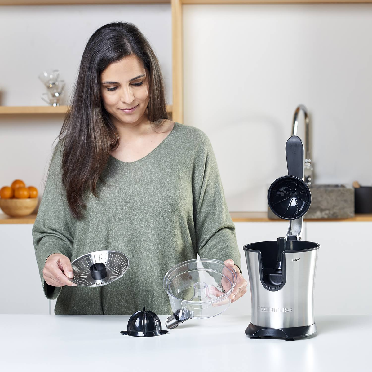 Una mujer usando una exprimidora. Sostiene un colador y un cuenco transparente.