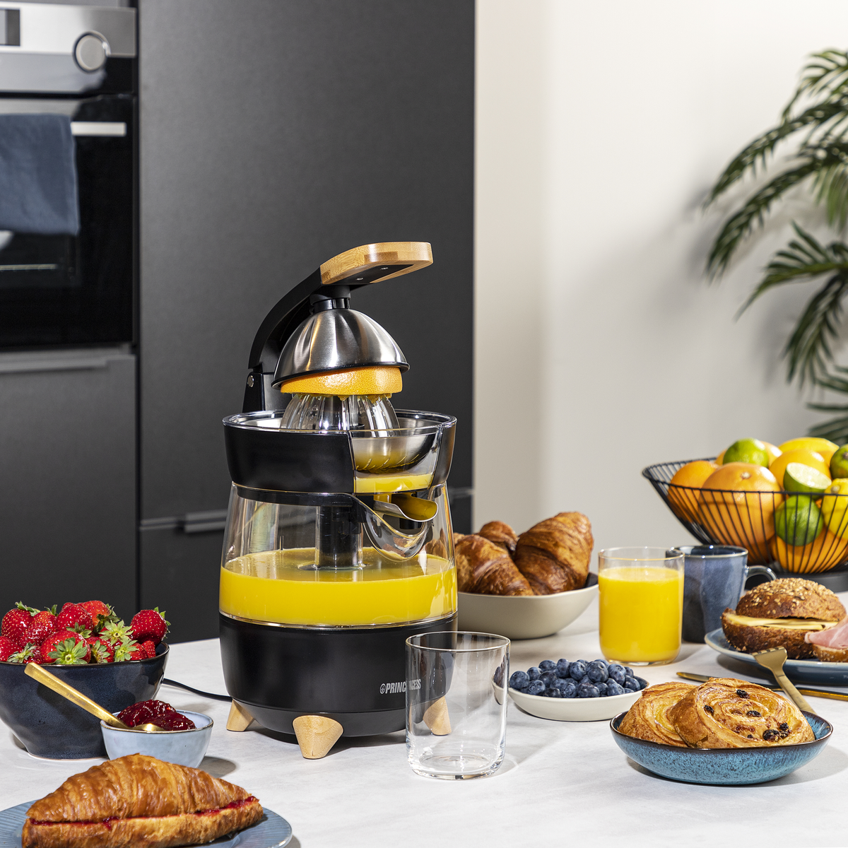 Srebrno-czarna wyciskarka z odłączanymi częściami. Wyciskarka i części znajdują się na białej powierzchni.