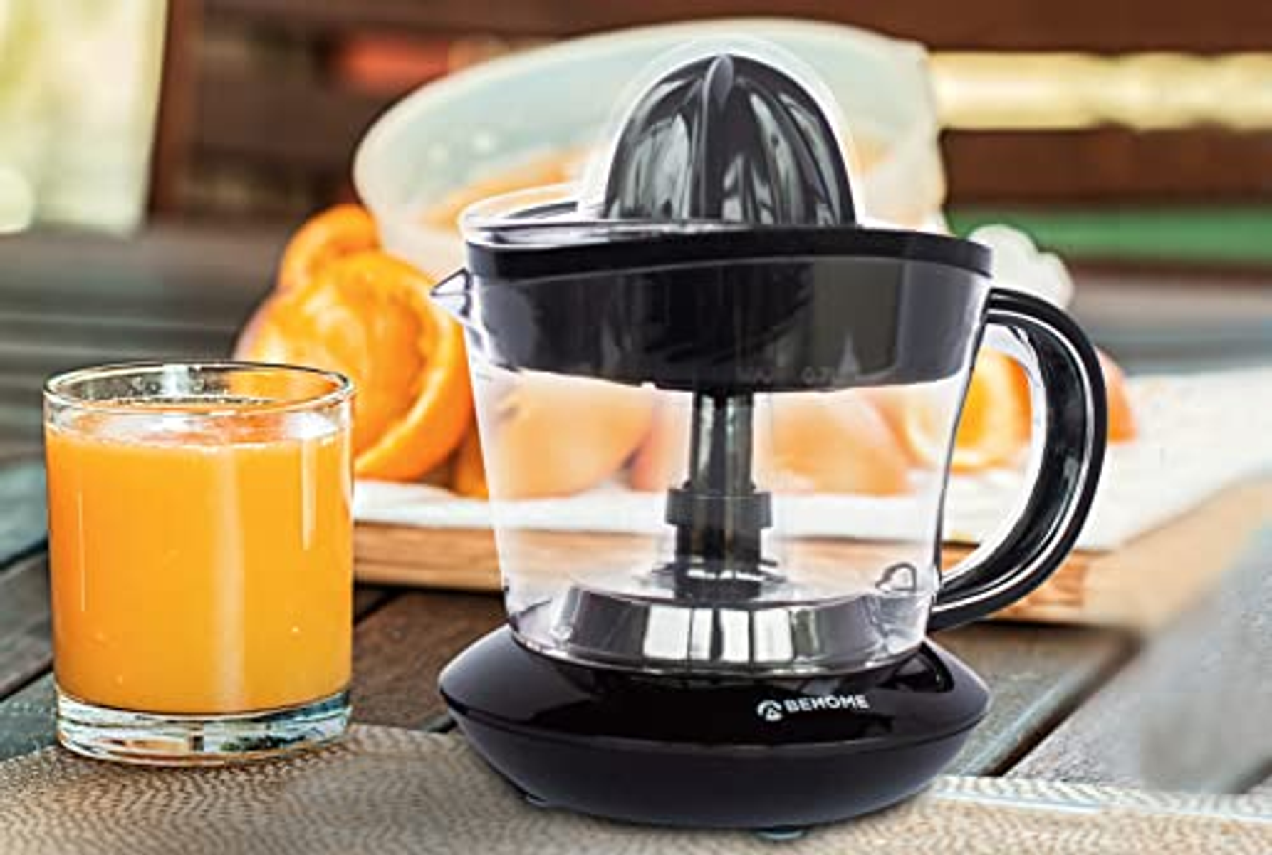 Spremiagrumi elettrico nero con succo d'arancia in un bicchiere e arance. Su un tavolo.