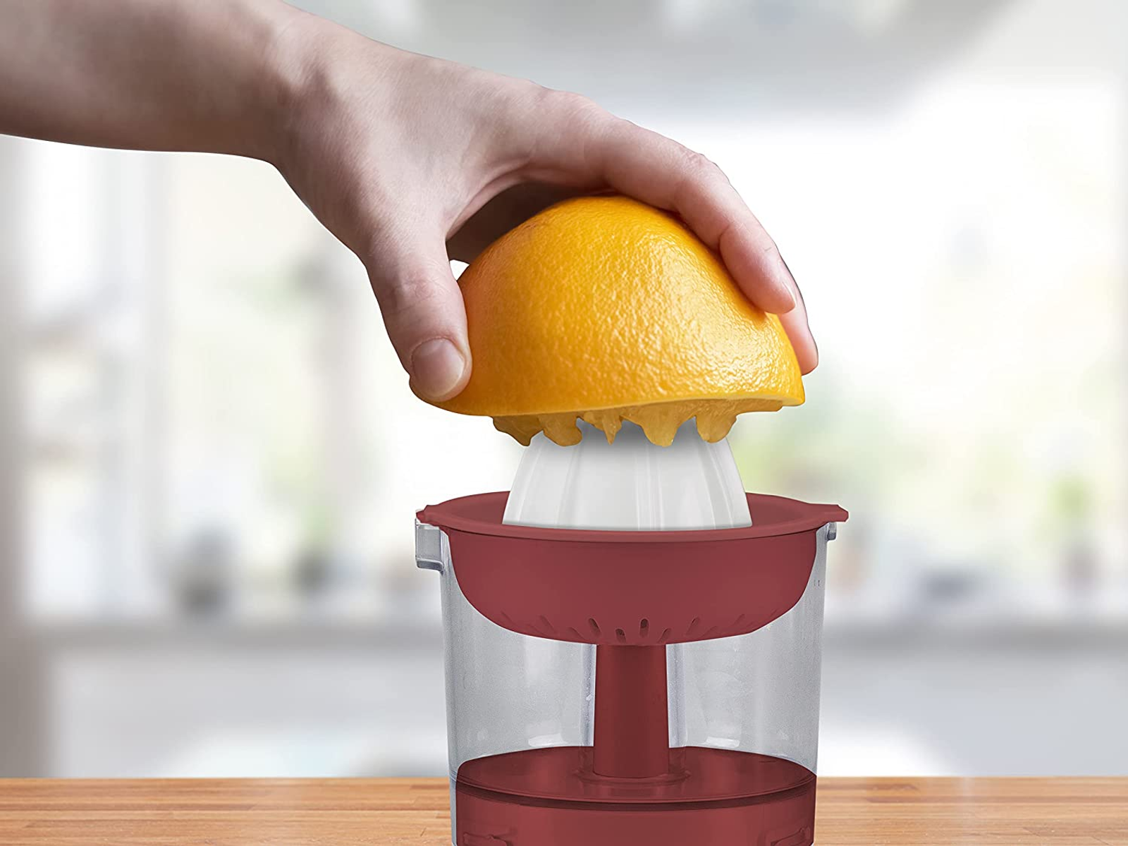 Una mano che spremi una metà di arancia su un reamer bianco in un contenitore di succo rosso.